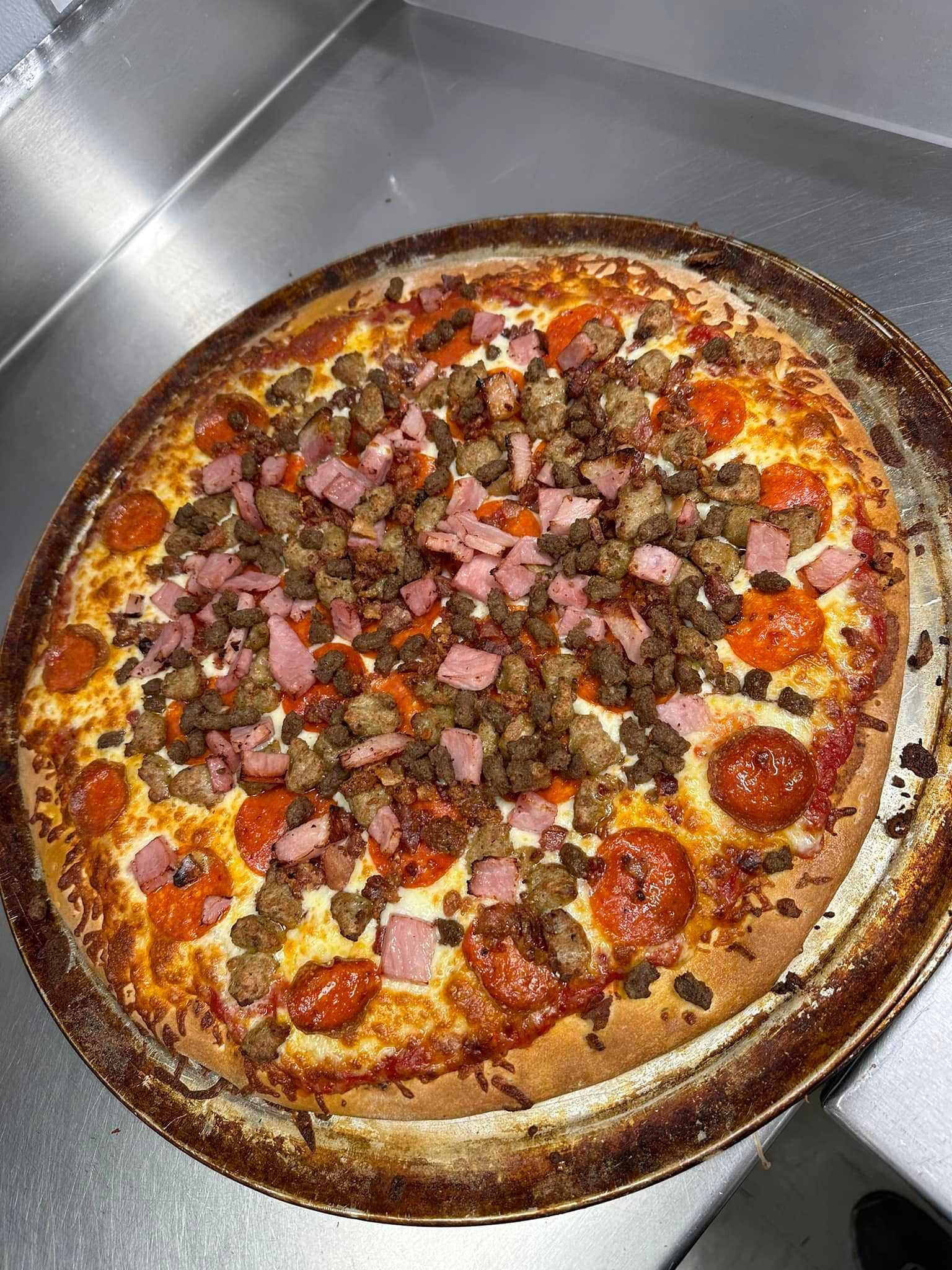 A freshly baked pizza topped with pepperoni, diced ham, and sausage on a kitchen counter.