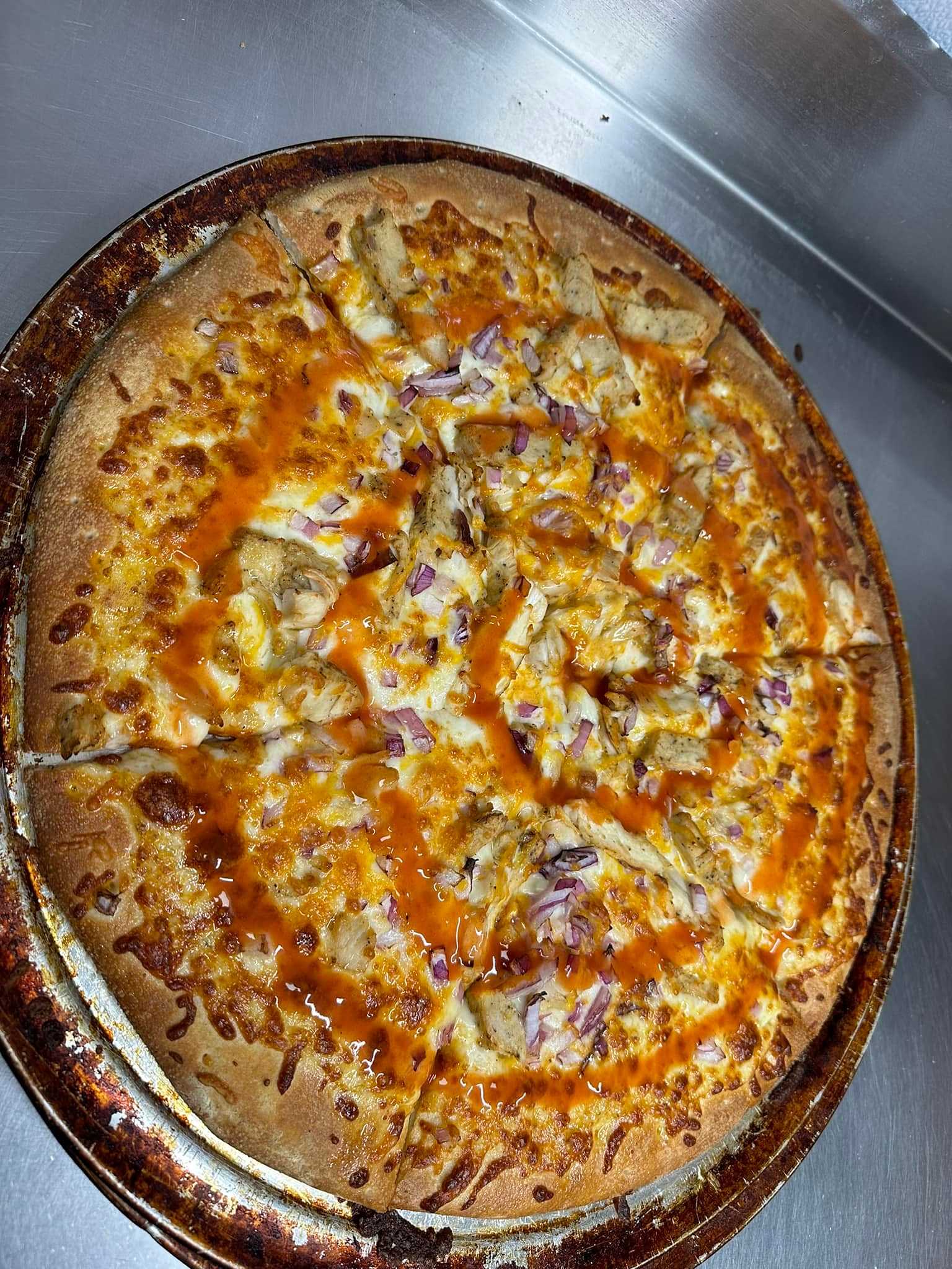 Buffalo chicken pizza with cheese, red onions, and a drizzle of hot sauce on a metal tray.