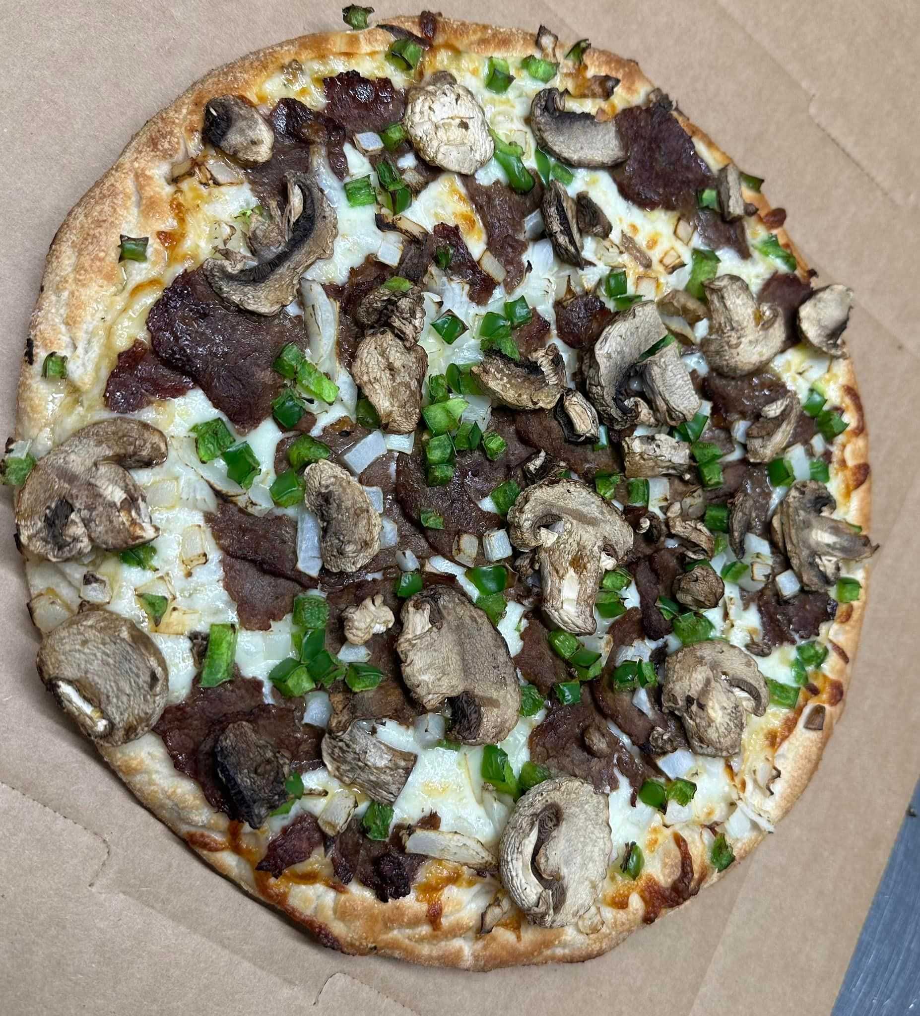 Pizza topped with mushrooms, green peppers, onions, and beef on a cardboard surface.