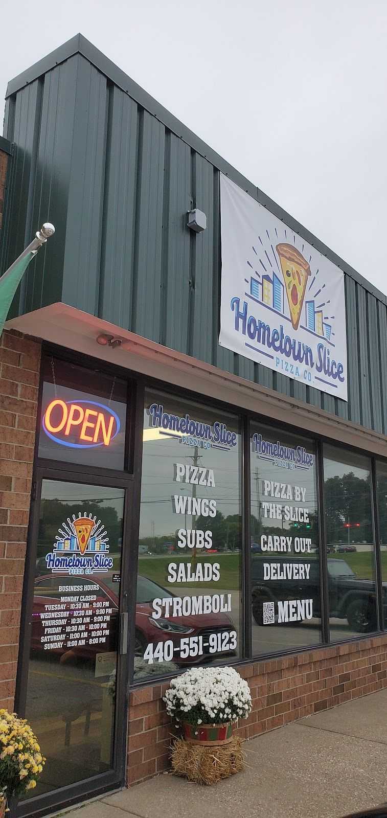 Storefront of Hometown Slice Pizza Co. with neon "OPEN" sign and menu details on window.