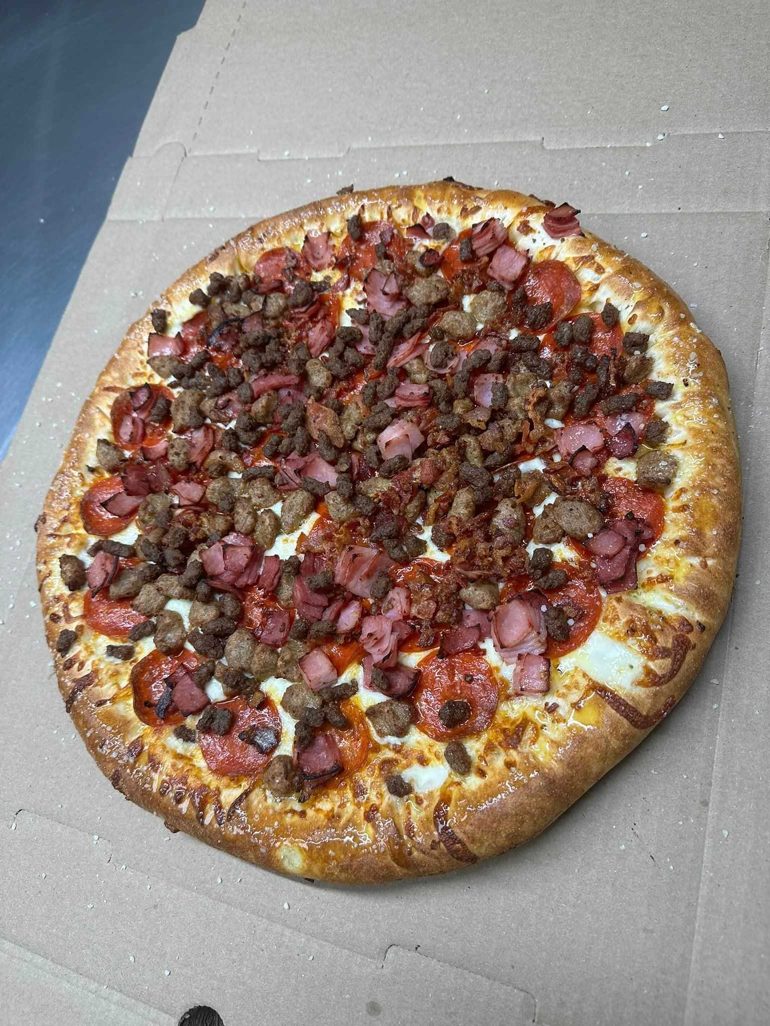 A freshly baked pizza topped with pepperoni, bacon, and sausage on a cardboard box.