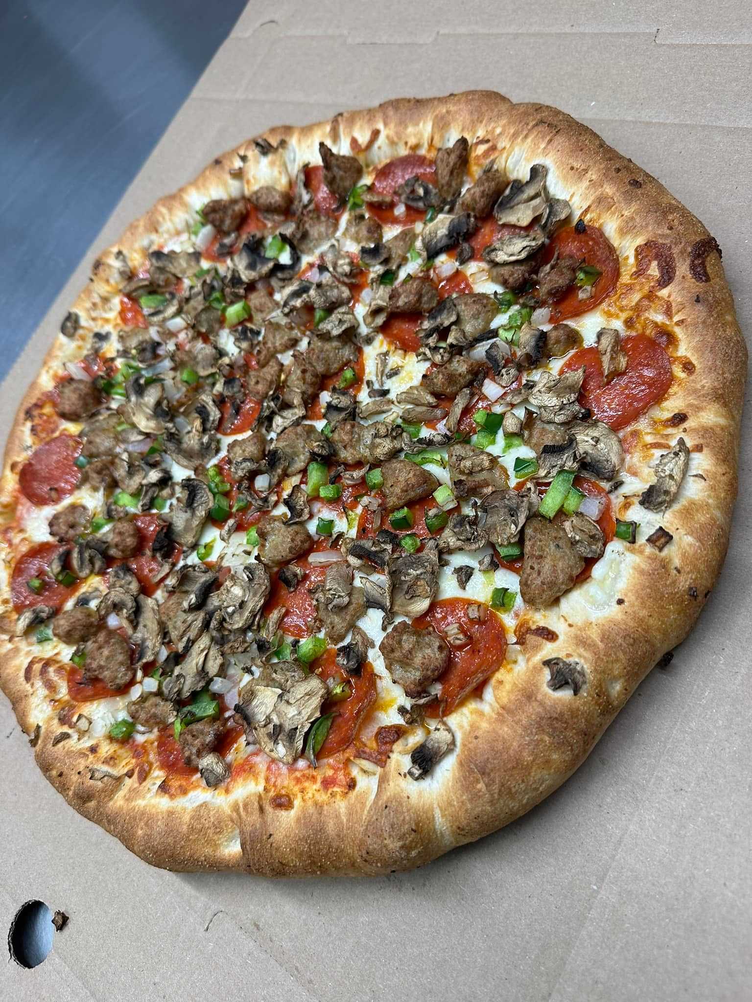 Pizza with mushrooms, sausage, green peppers, and pepperoni on a cardboard surface.