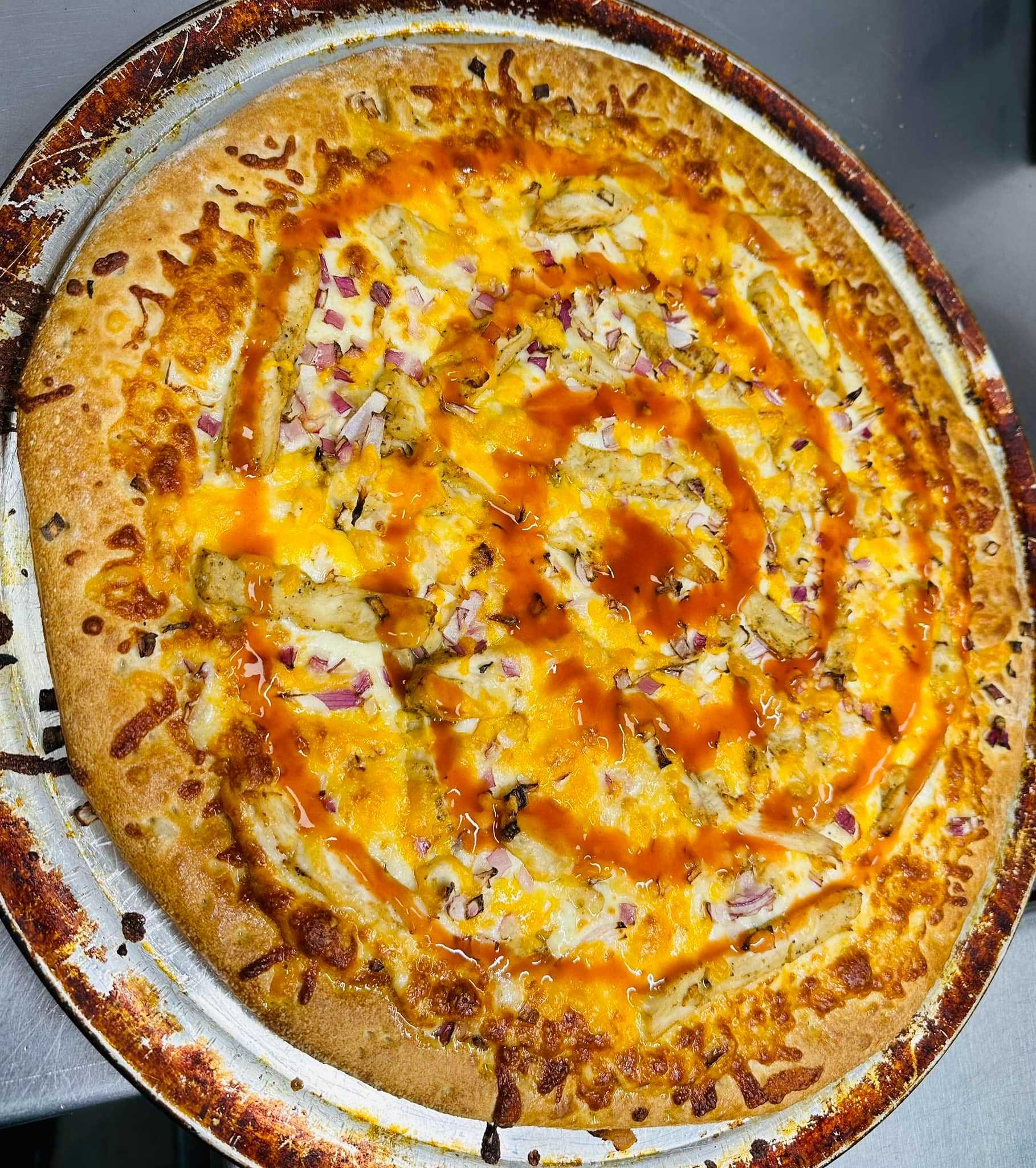 Cheese pizza with buffalo sauce drizzle, red onions, and light char marks on a metal tray.